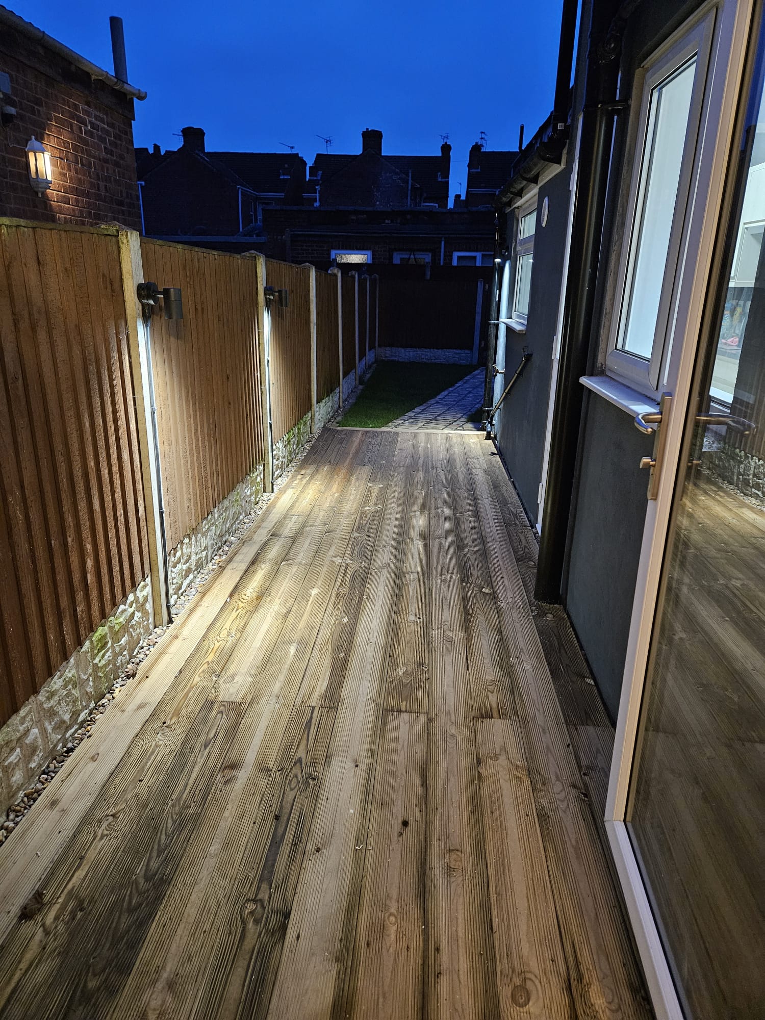 Long timber deck at dusk, fence-mounted lights illuminating the path