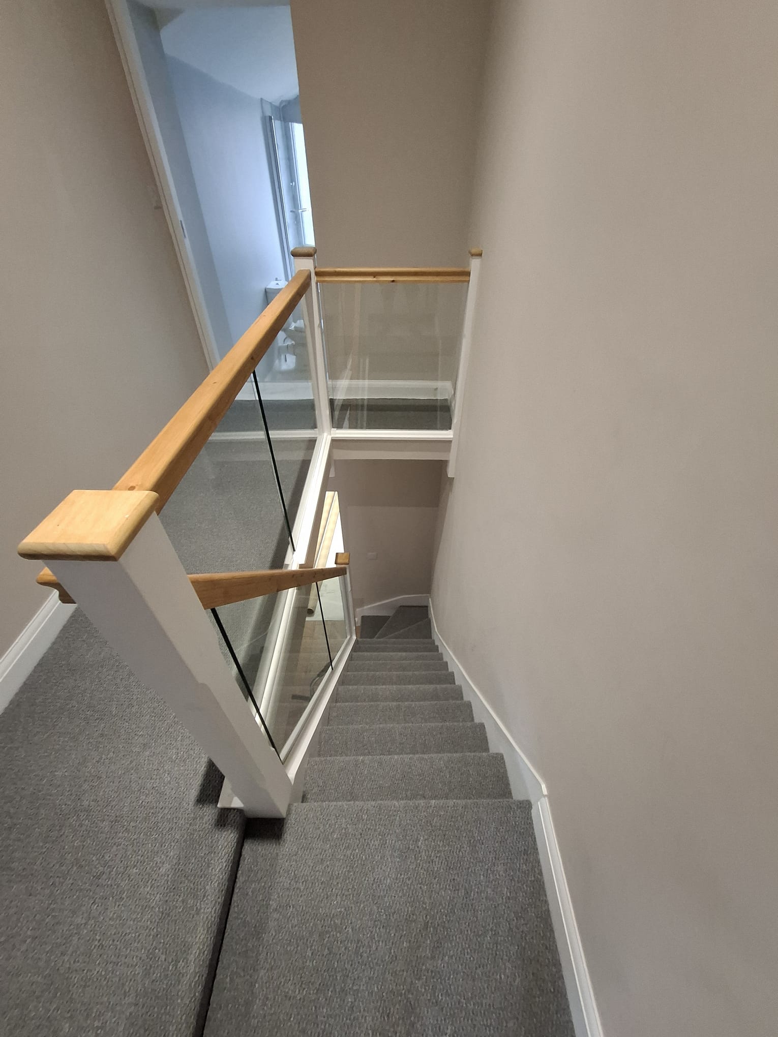 Refurbished staircase with oak handrails, glass balustrade and grey carpet