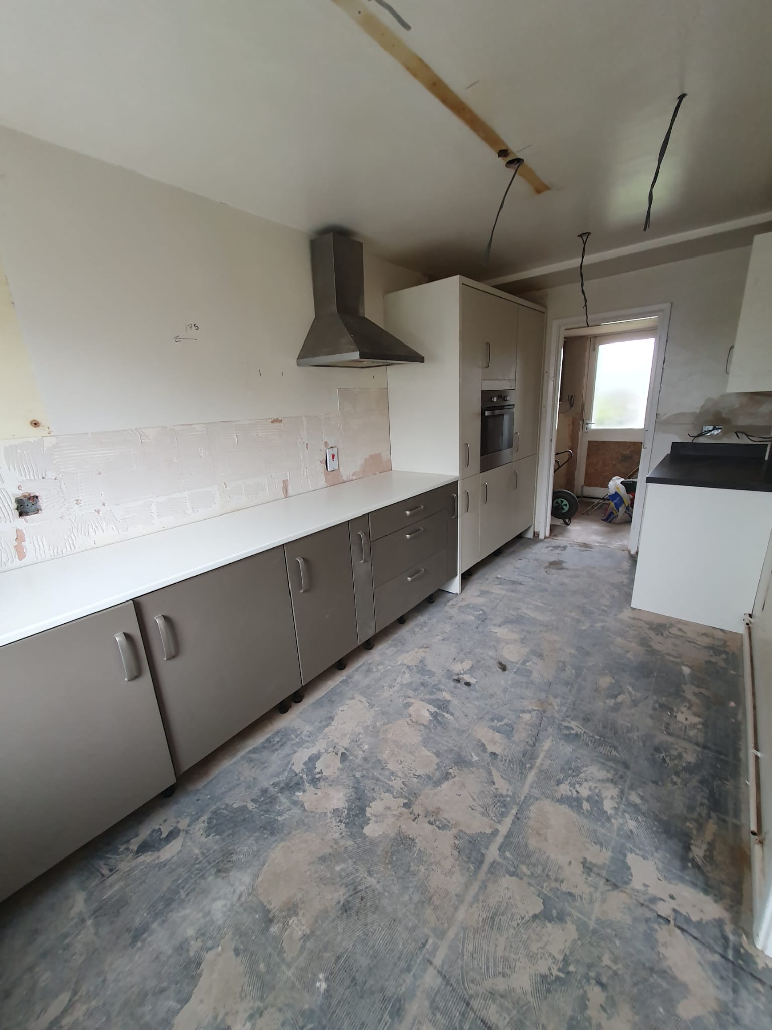 New galley kitchen mid-fit with grey base units, white worktops and chimney hood