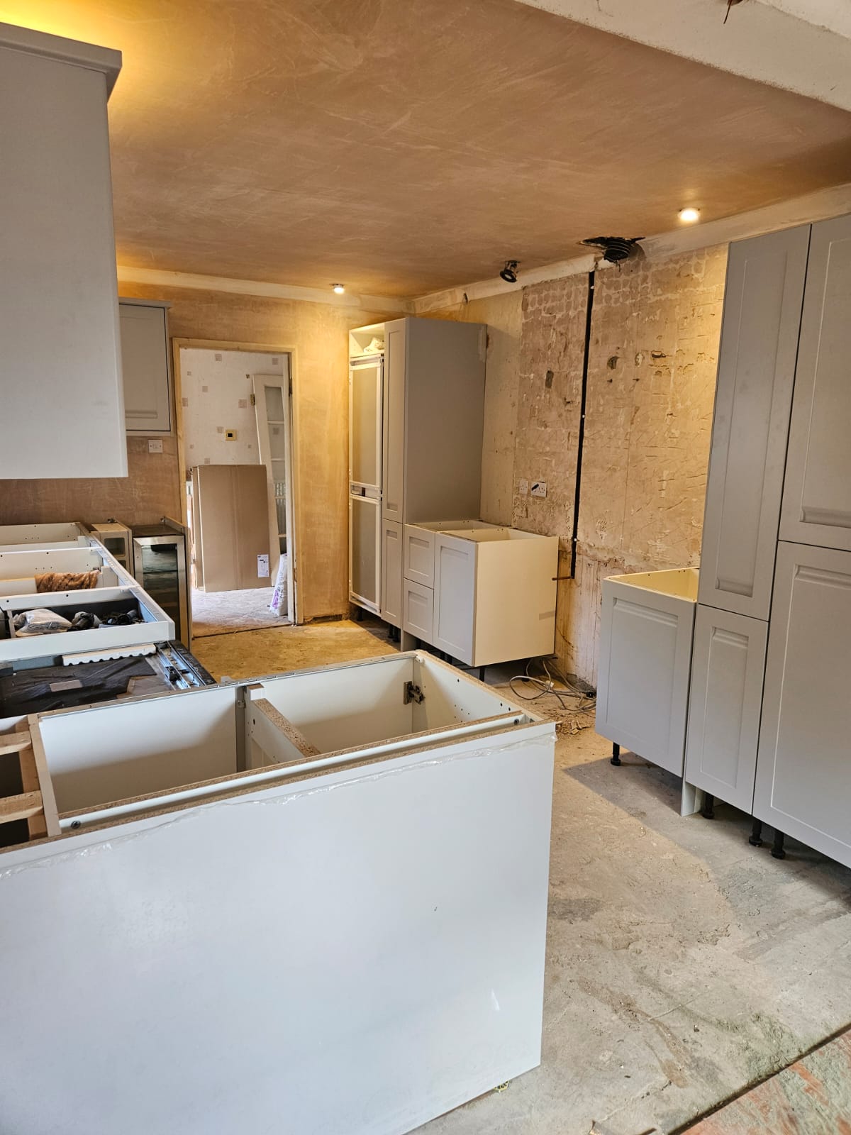 Grey shaker kitchen mid-fit with base and tall units part-installed, freshly plastered ceiling and stripped-back wall