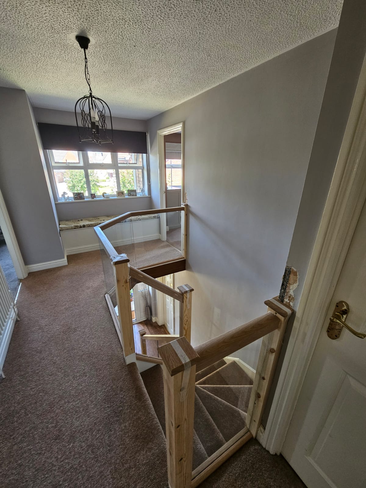 Refurbished staircase and landing with oak handrails, glass balustrade panels and grey carpet